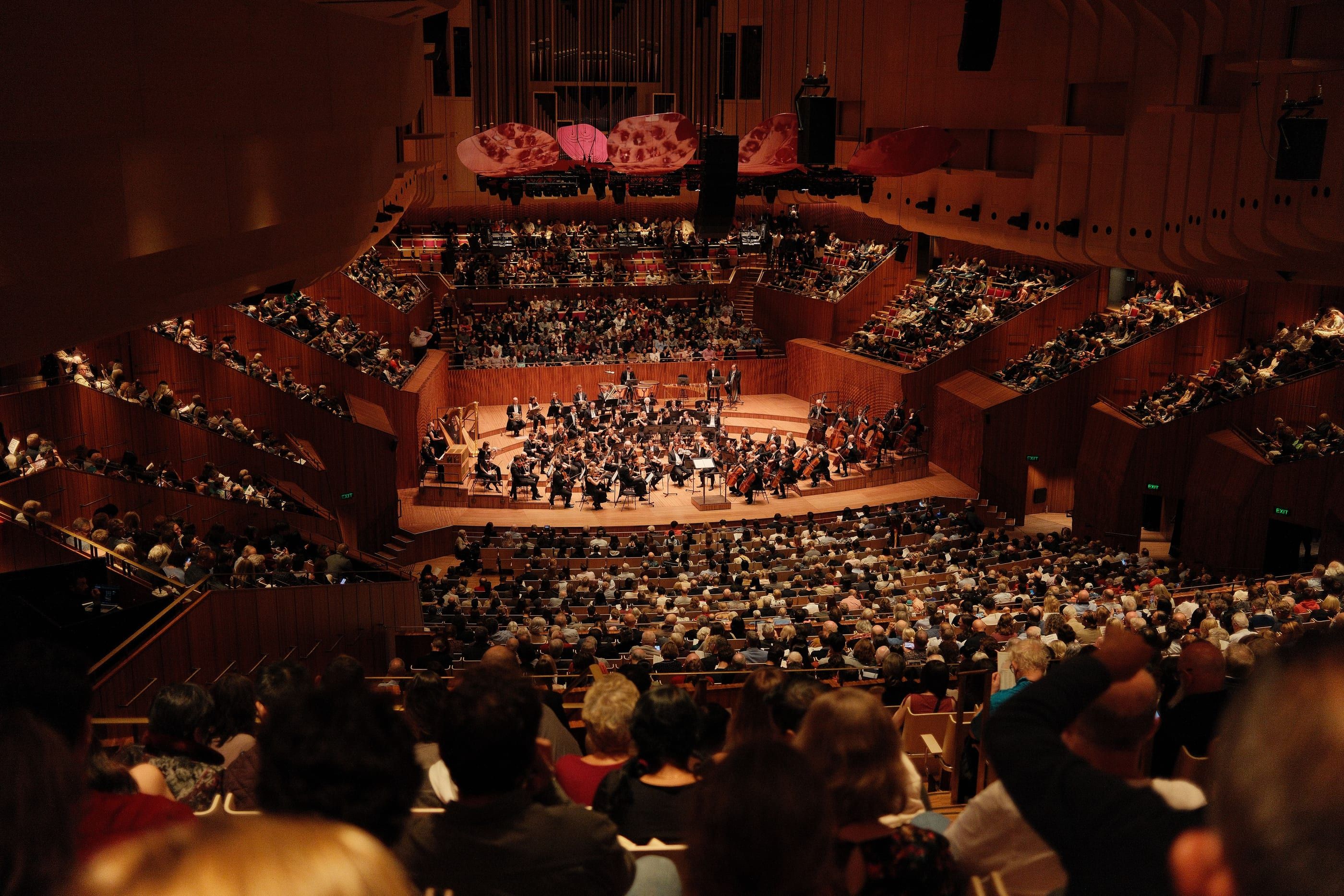 Ein Symphonieorchester vor vollem Konzertsaal, gesehen aus den oberen Reihen.