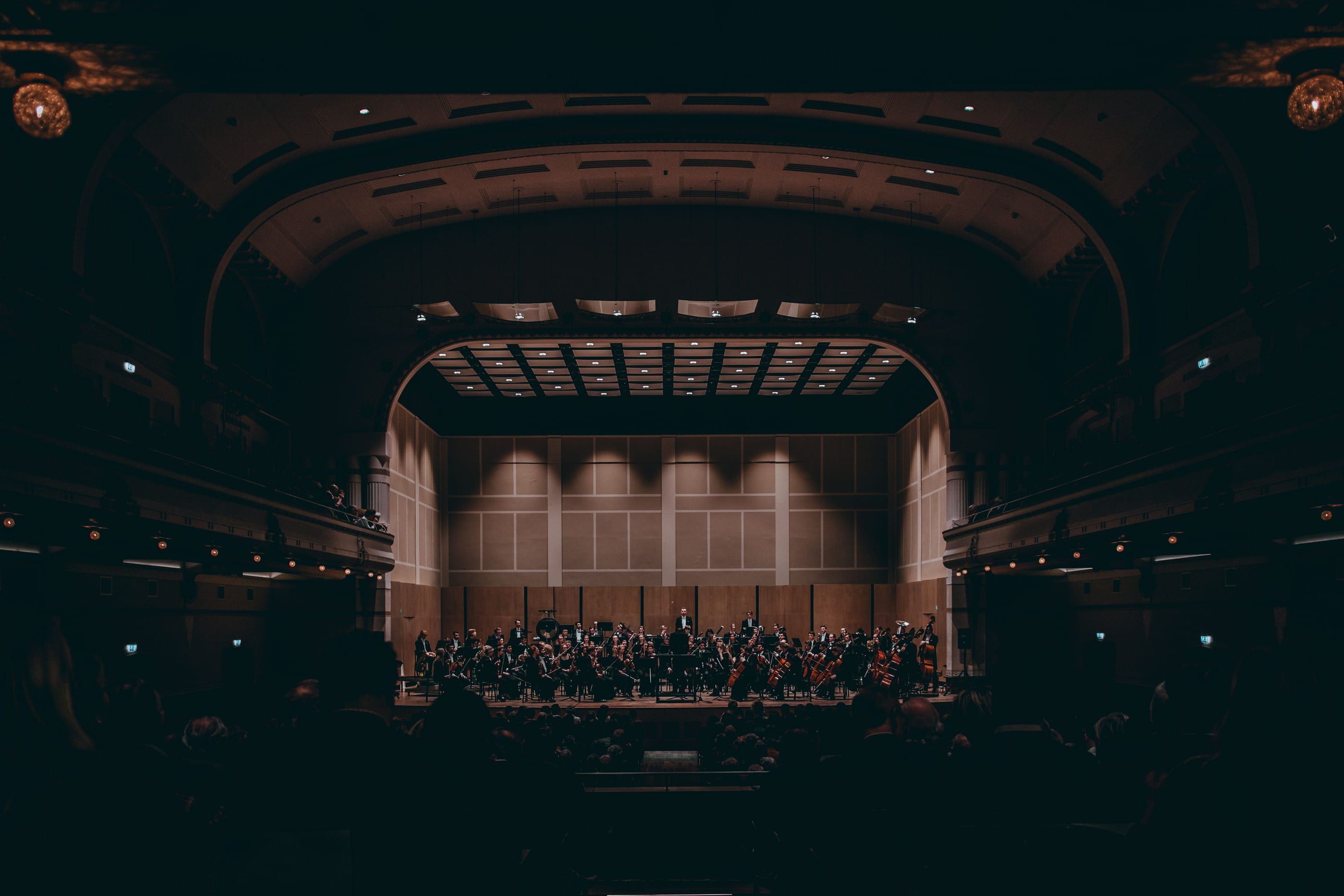Ein Symphonieorchester auf einer warm beleuchteten Bühne in einem abgedunkelten Konzertsaal.